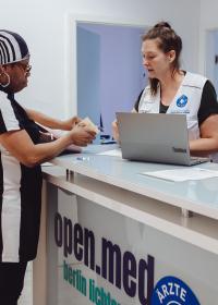 Eine Ärzte der Welt Mitarbeiterin gibt einer Patientin eine Visitenkarte in der open.med Praxis Berlin. Foto: Max Avdeev