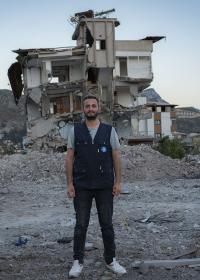 Ein Mitglied des Teams von Ärzte der Welt steht vor einem Gebäude, das bei dem Erdbeben in der Region Hatay in der Türkei zerstört wurde. Foto: Huseyin Aldemir