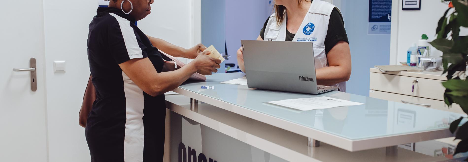 Eine Ärzte der Welt Mitarbeiterin gibt einer Patientin eine Visitenkarte in der open.med Praxis Berlin. Foto: Max Avdeev