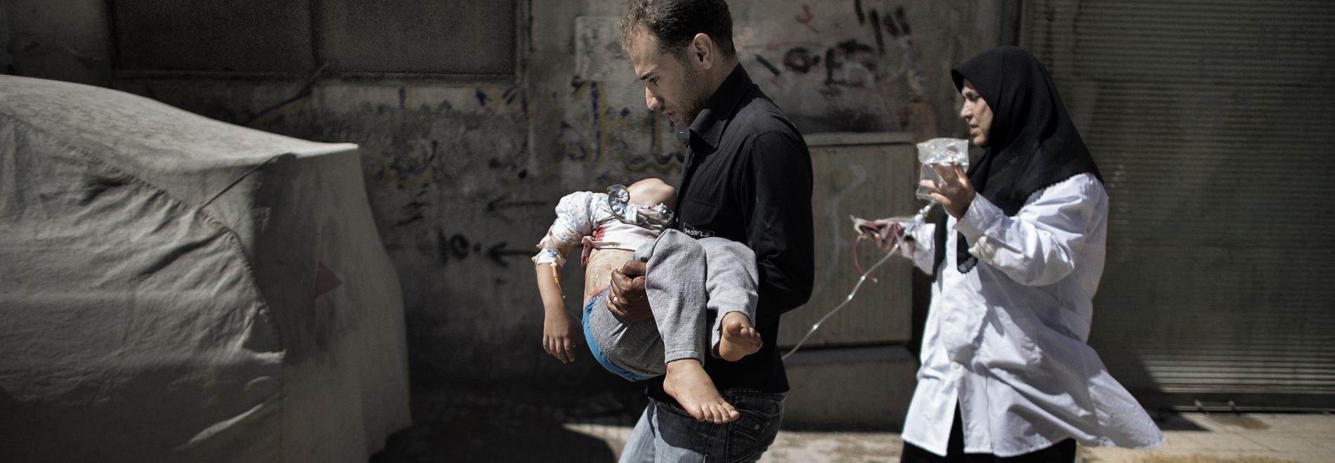 Ein Vater trägt sein Kind, das bei einem Bombenangriff verletzt wurde. Foto: Marco Longari, AFP