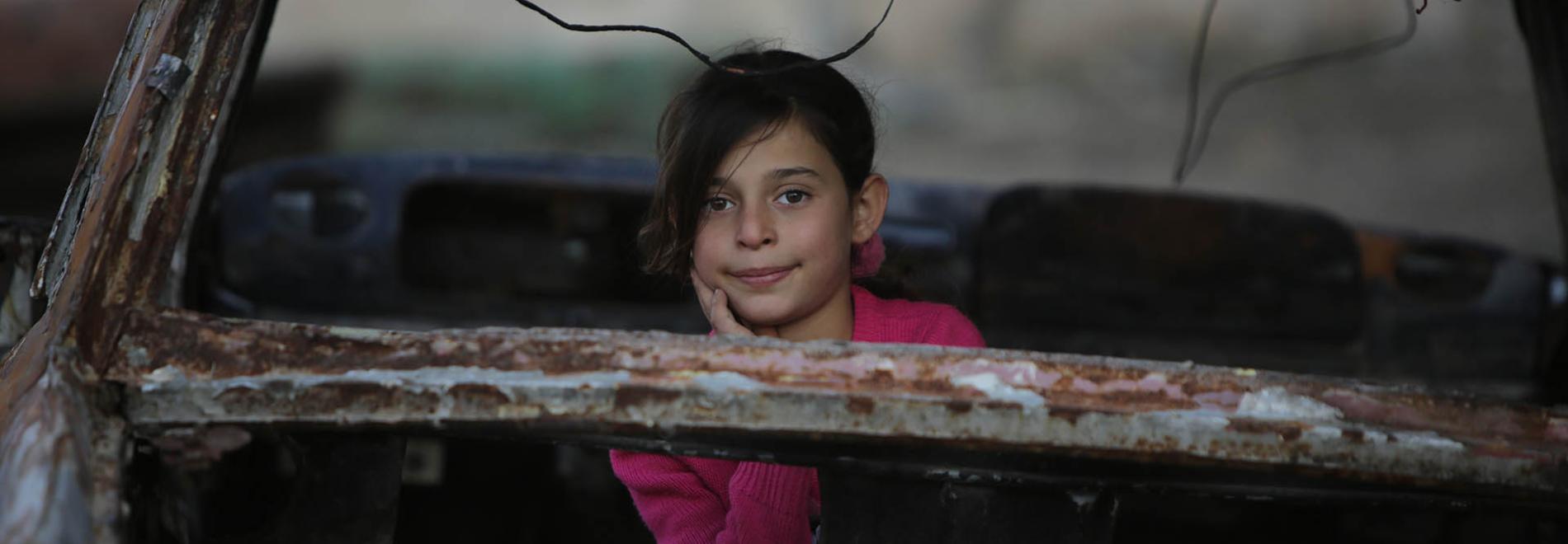 Ein junges Mädchen spielt in den Überresten eines Fahrzeugs, das durch die Kämpfe in Syrien zerstört wurde. Foto: Ärzte der Welt (DDD)