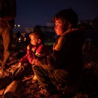 Kinder, deren Zuhause durch das Erdbeben 2023 an der türkisch-syrischen Grenze zerstört wurde, wärmen sich an einem Holzfeuer in einem provisorischen Lager. Foto: Olivier Papegnies