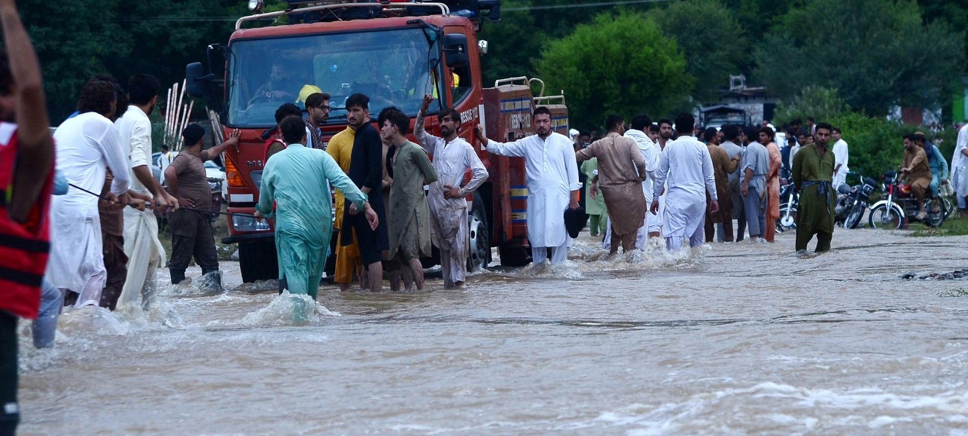 Menschen in Pakistan stehen auf einer überfluteten Straße bei einem Rettungsfahrzeug. Foto: Hussain Ali