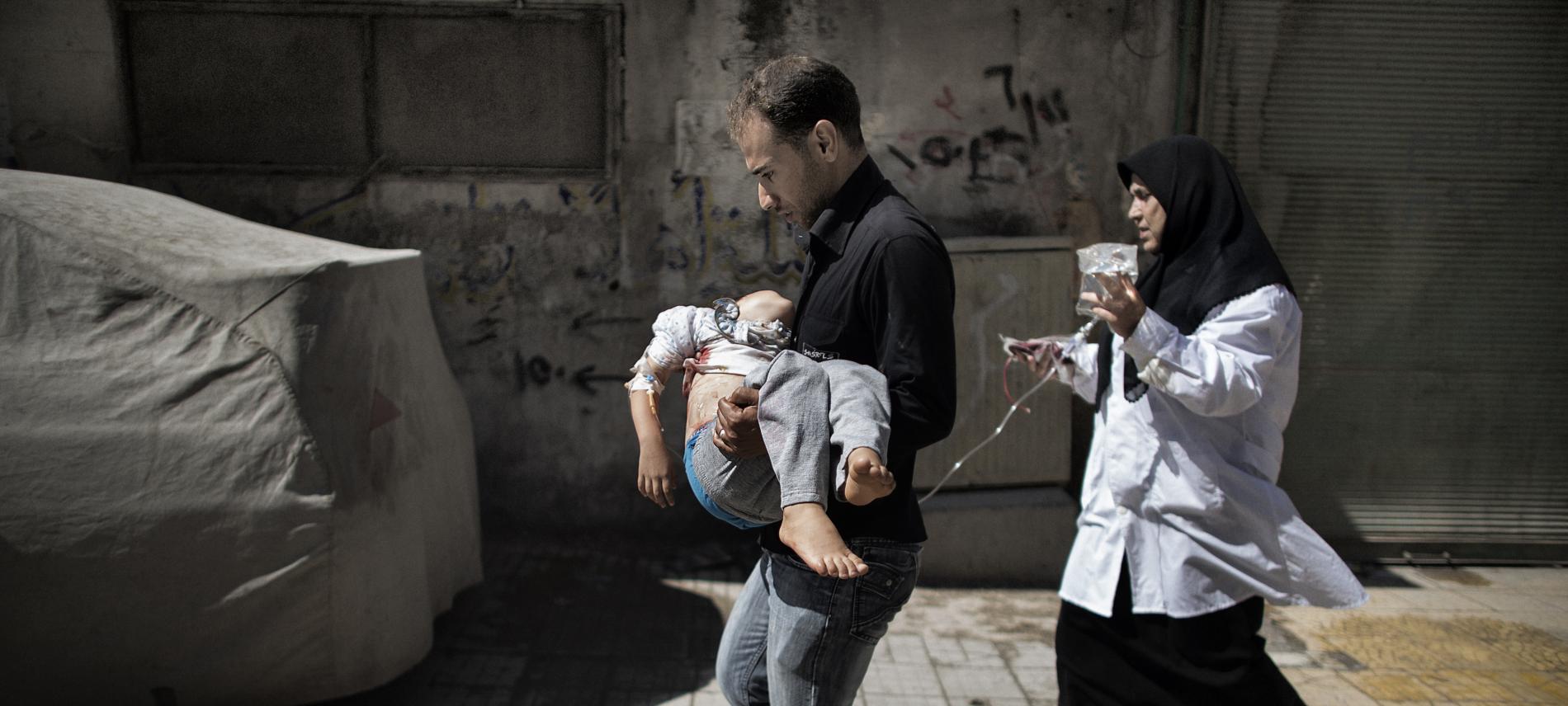 Ein Vater trägt sein Kind, das bei einem Bombenangriff verletzt wurde. Foto: Marco Longari, AFP