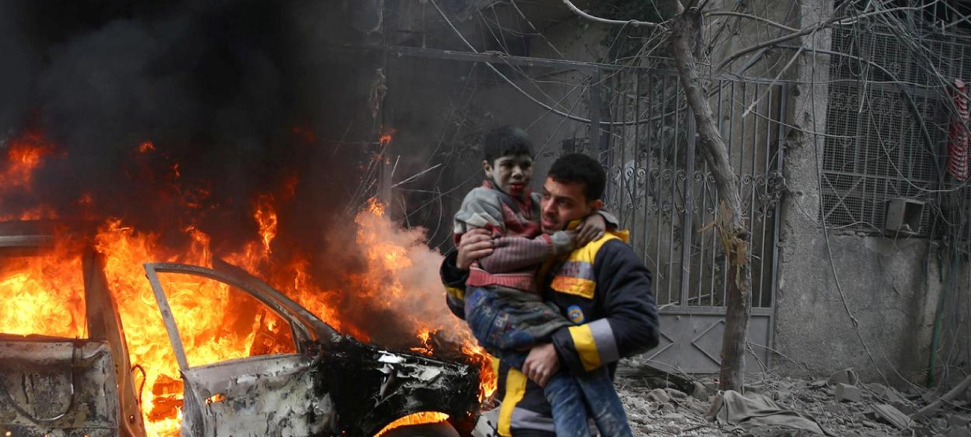 Ein Helfer trägt ein verletztes syrisches Kind  Ein Mann mit einem Kind auf dem Arm vor einem brennenden Auto