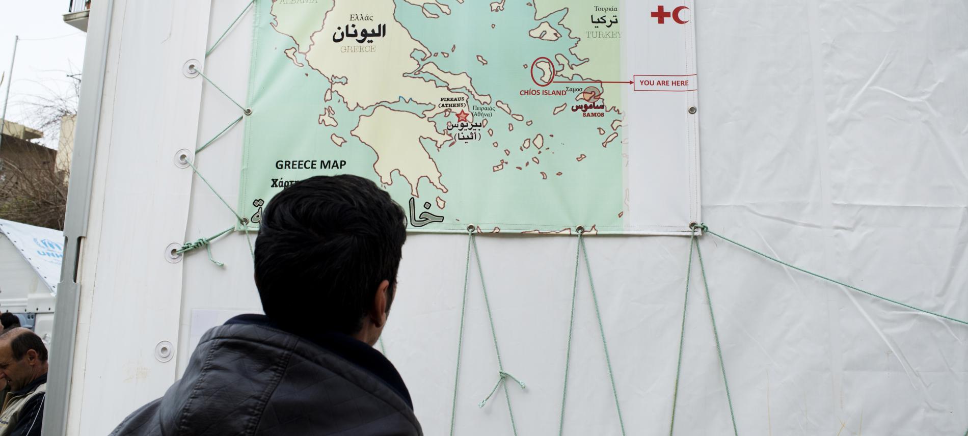  Ein Flüchtling betrachtet eine Landkarte, auf der die Insel Chios markiert ist.