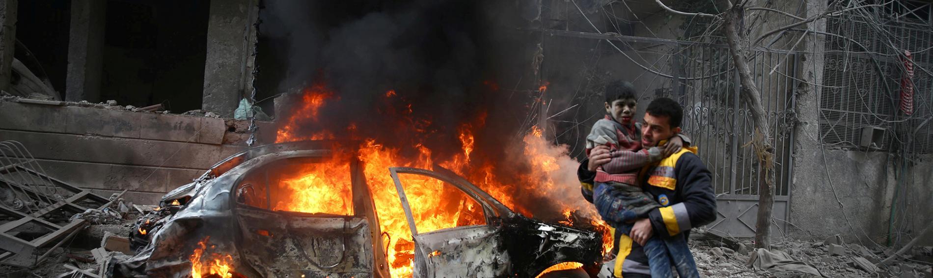 Ein Mann mit einem Kind auf dem Arm vor einem brennenden Auto
