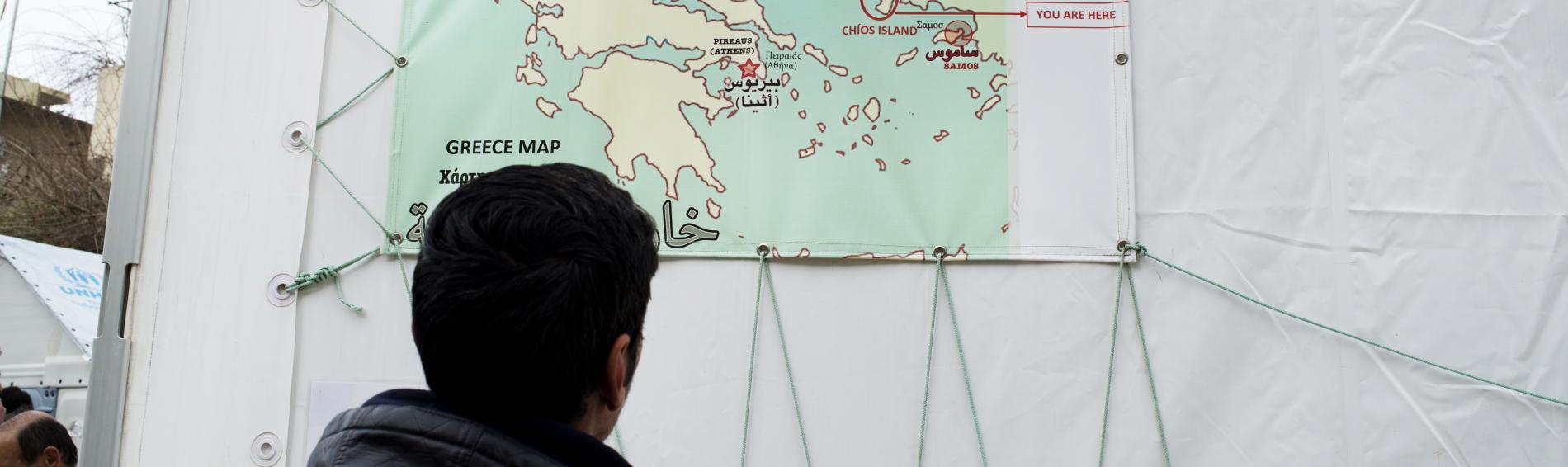  Ein Flüchtling betrachtet eine Landkarte, auf der die Insel Chios markiert ist.