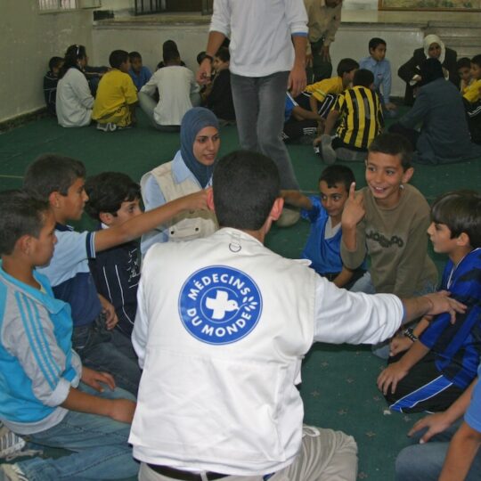 Gaza: Eine Gruppe von Kindern sitzt in einem Kreis und wird von einem Angestellten von Ärzte der Welt betreut.