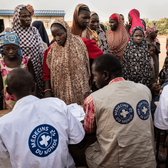 Frauen und Kinder stehen vor Mitarbeitern von Ärzte der Welt. © Kristof Vadino
