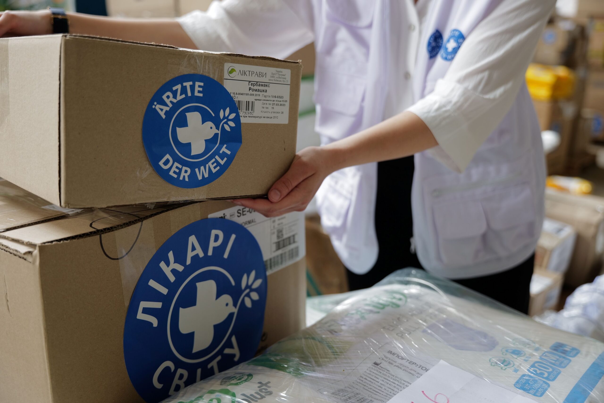 Ukraine: Auf einem Tisch liegt ein Paket von Ärzte der Welt und eine Mitarbeiterin hebt ein weiteres Paket an, um es darauf zu legen. © Till Mayer