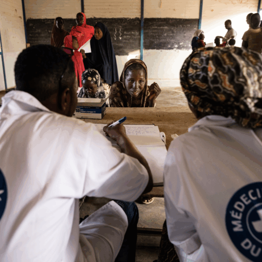 Zwei Mitarbeiter von Ärzte der Welt beraten eine Frau in Niger. Sie sitzen sich gegenüber an einem Tisch. ©Kristof Vadino Title Tag: ©Kristof Vadino