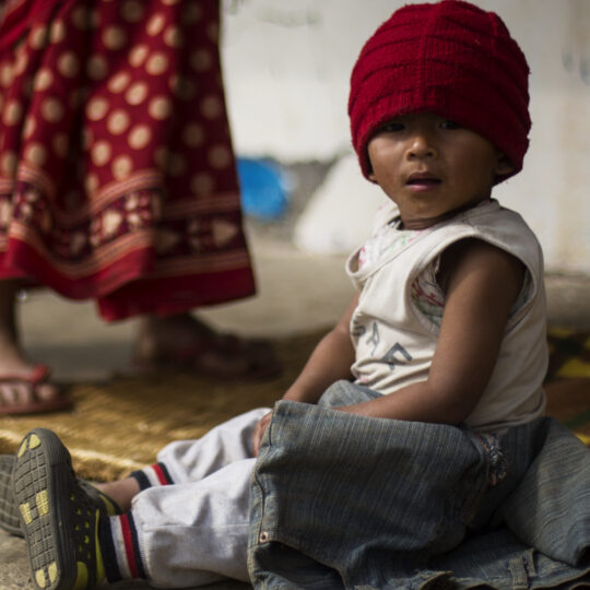 Nepal: Ein kleiner Junge mit roter Mütze sitzt auf dem Boden. © Ärzte der Welt