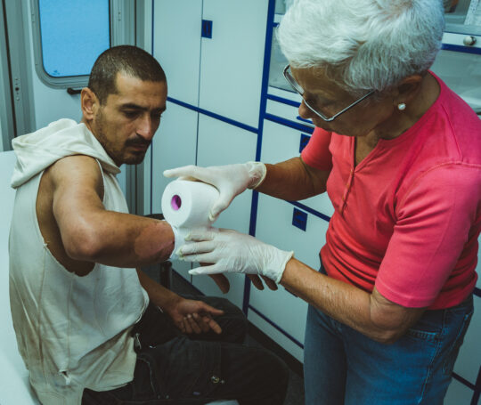 Ein Einsatz im MedMobil in Stuttgart: Eine Ehrenamtliche verbindet einem Mann eine Wunde. © David Gohlke