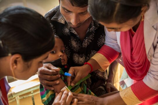 Bangladesch: Ein Mann hält seinen Sohn auf dem Arm. Eine Mitarbeiterin von Ärzte der Welt misst den Armumfang des Jungen. © Ärzte der Welt