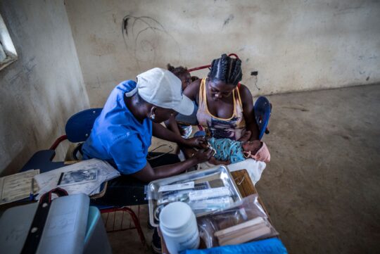 Eine Mitarbeiterin von Ärzte der Welt impft ein Baby in Haiti, das in den Armen seiner Mutter liegt. © Ärzte der Welt