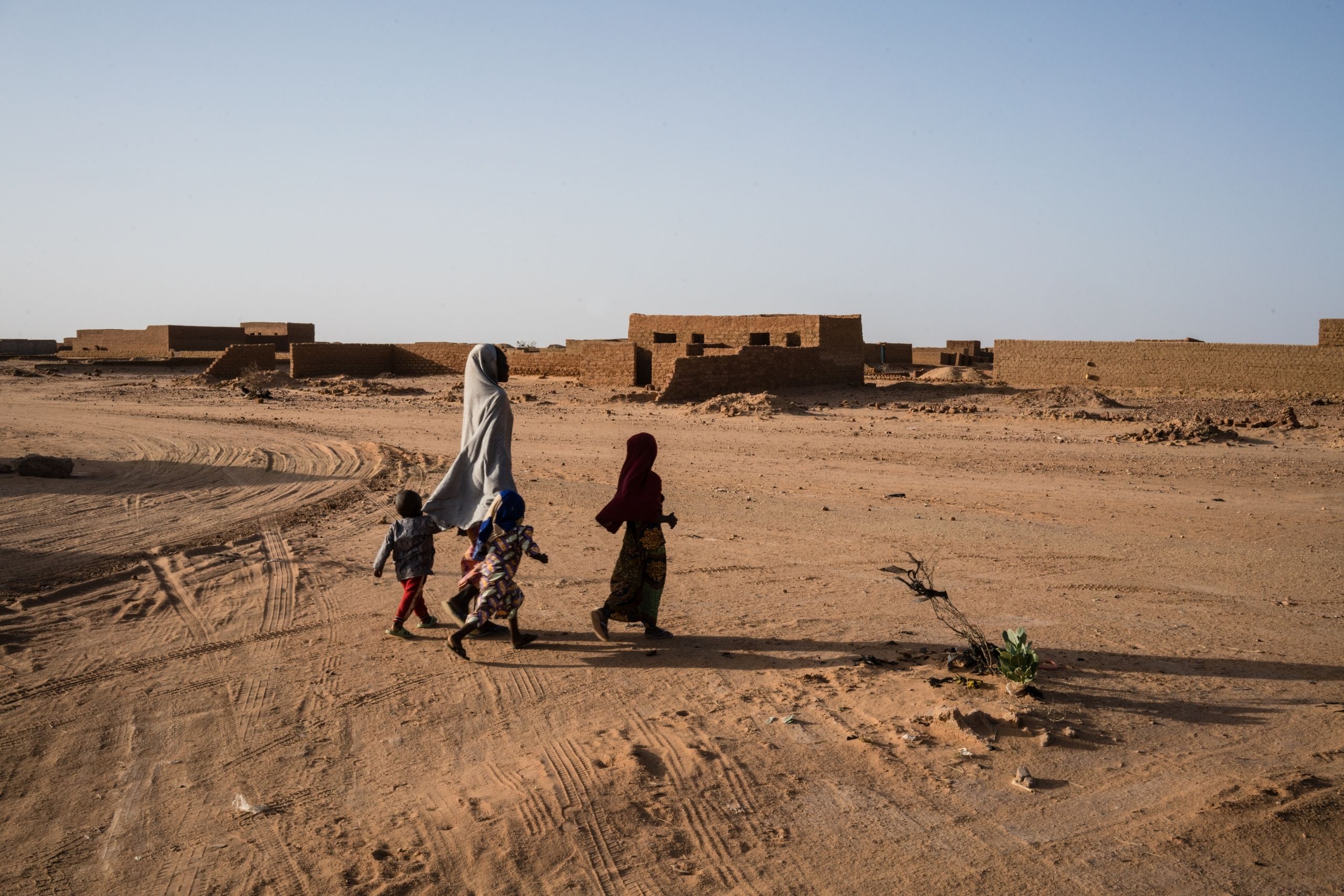 Niger: Eine Mutter mit zwei Kinder läuft durch eine sandige Landschaft nahe Agadez. © Kristof Vadino