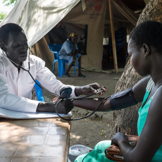 Ein medizinischer Angestellter misst einer Patientin den Blutdruck. © Bruno Abarca