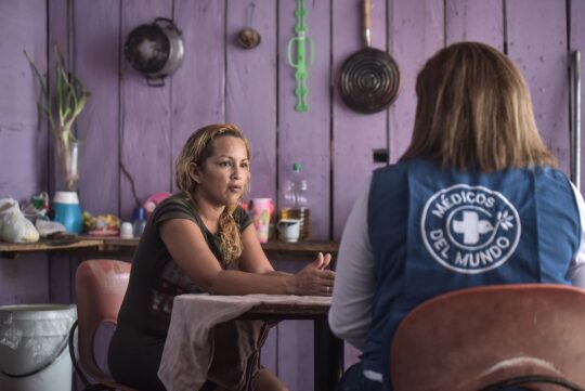 Eine Mitarbeiterin und eine Kolumbianerin sitzen an einem Tisch und unterhalten sich. © Quentin Top