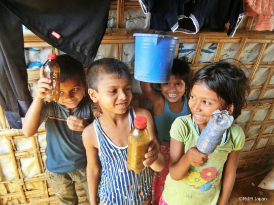 Bangladesch: Eine Gruppe Kinder steht lachend zusammen und hält Flaschen hoch. © Ärzte der Welt