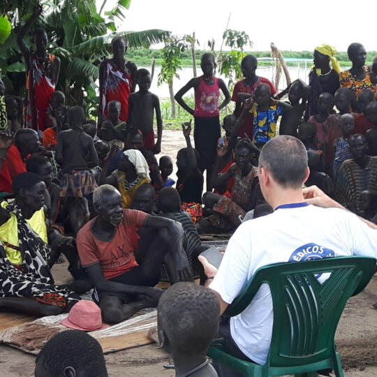 Südsudan: Zwei Mitarbeiter*innen sprechen mit einer Gruppe von Menschen. © Bruno Abarca