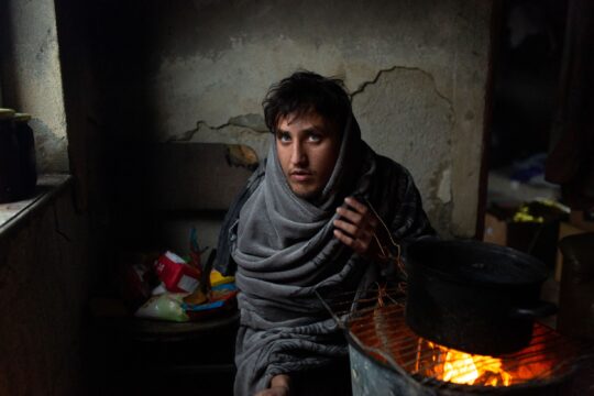 Bosnien: Ein Mann sitzt in einer Decke eingewickelt an einem Feuer in einem heruntergekommenen Zimmer. © Michele Lapini