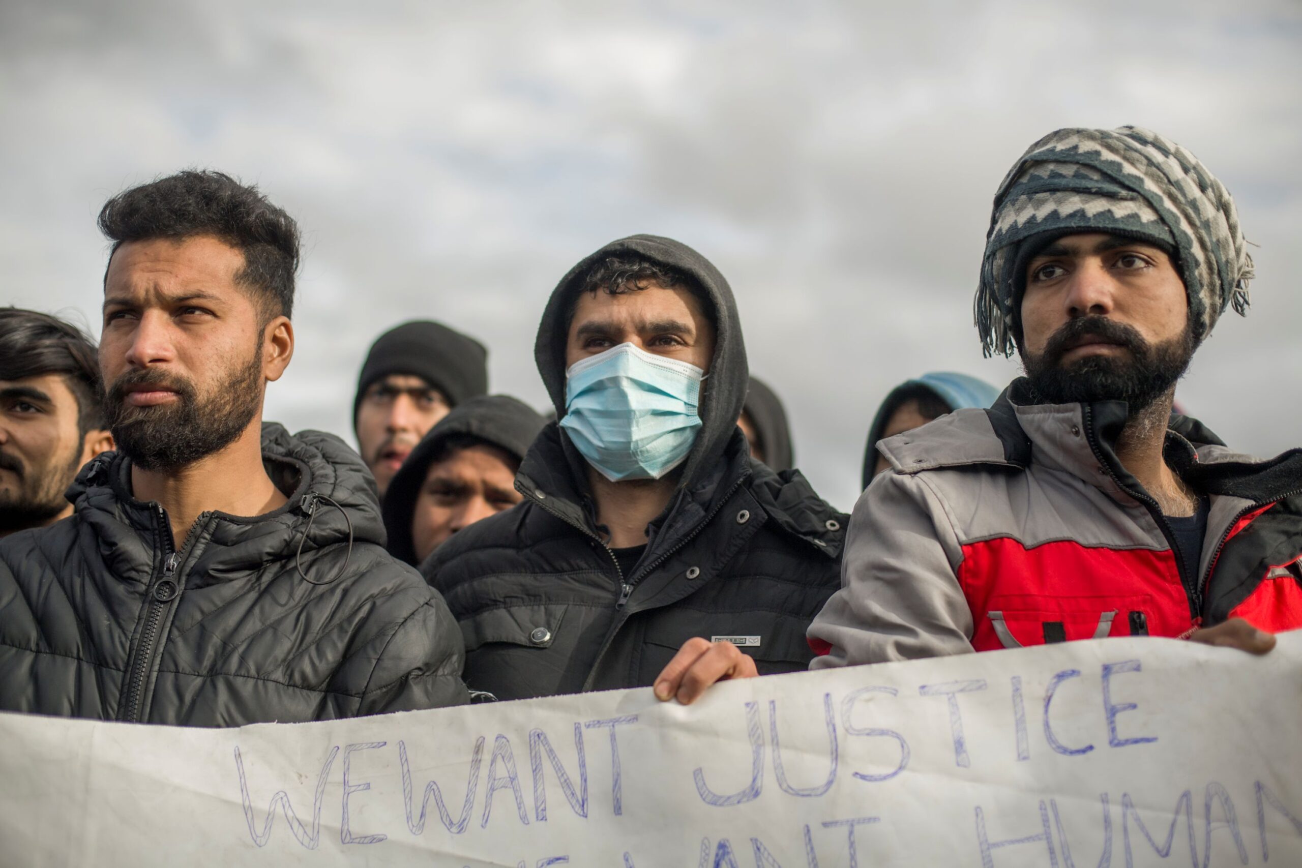 Bosnien: Mehrere Männer demonstrieren für Gerechtigkeit. Sie halten ein Schild und schauen in die Ferne. © Michele Lapini