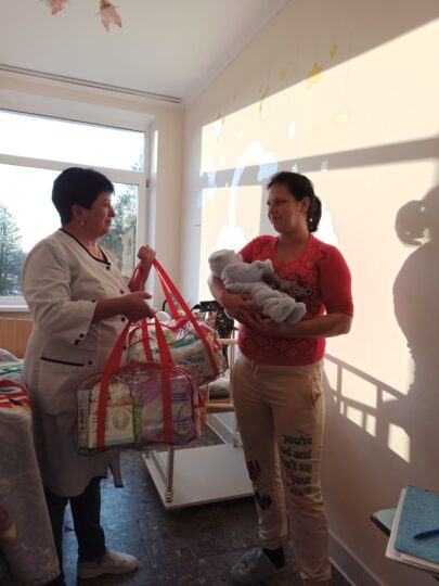 Eine Mitarbeiterin von Ärzte der Welt überreicht einer ukrainischen Mutter mit einem Baby im Arm ein Paket mit Ausstattung für Neugeborene. © Ärzte der Welt