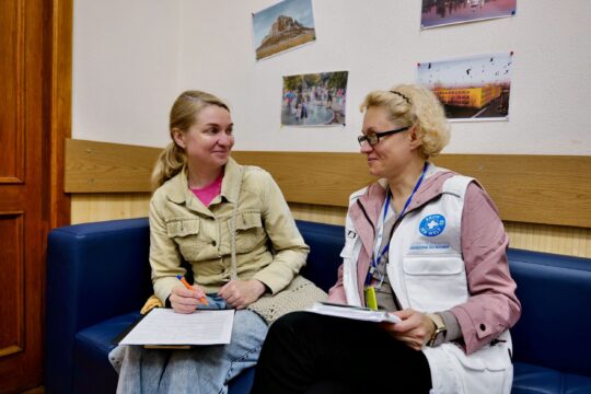 Ukraine: Eine Mitarbeiterin von Ärzte der Welt und eine Patientin sitzen auf einem Sofa und schauen sich lächelnd an. © Till Mayer