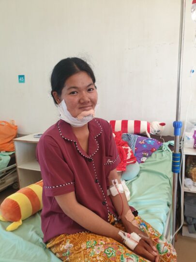 Operiertes Mädchen sitzt in Kambodscha lächelnd auf einem Krankenhausbett. © Ärzte der Welt