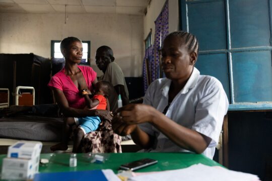 DR Kongo: Ein Mitarbeiter von Ärzte der Welt bereitet eine Impfung vor. Hinter ihm sitzt eine Familie mit einem Kind. © Alexis Aubin