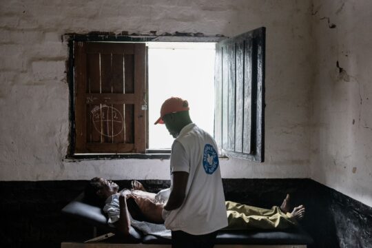 DR Kongo: Ein Mitarbeiter von Ärzte der Welt untersucht einen Mann auf einer Liege am Körper, der sein Gesicht vor Schmerzen verzieht. © Alexis Aubin