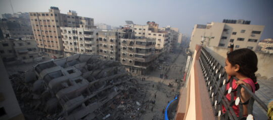 Ein Kind schaut über ein Geländer auf ein zerstörtes Gebiet in Gaza.