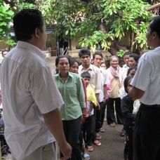 Zwei Ärzte von Ärzte der Welt stehen mit dem Rücken zur Kamera vor einigen Leuten. © Ärzte der Welt