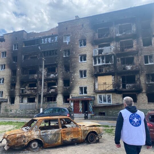 Ukraine: Ein Mitarbeiter von Ärzte der Welt vor einem zerstörten und ausgebrannten Gebäude.