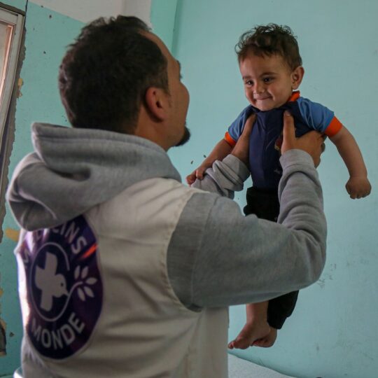 Gaza: Ein Mitarbeiter von Ärzte der Welt hebt ein lachendes Kind hoch. Ärzte der Welt leistet medizinische Nothilfe im Gazakrieg.