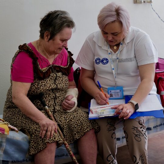 Ukraine: Eine Mitarbeiterin von Ärzte der Welt füllt gemeinsam mit einer Patientin ein Formular aus. Die Patientin hat eine verbundene Hand.