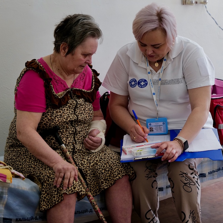 Ukraine: Eine Mitarbeiterin von Ärzte der Welt füllt gemeinsam mit einer Patientin ein Formular aus. Die Patientin hat eine verbundene Hand.