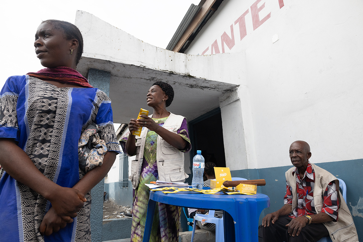 Drei Personen stehen und sitzen um einen Tisch mit Informationsmaterial