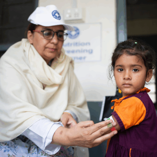 Ein kleines Mädchen wird in Pakistan von einer Ärztin von Ärzte der Welt auf Mangelernährung untersucht. Das Mädchen guckt in die Kamera. ©Saiyna Bashir