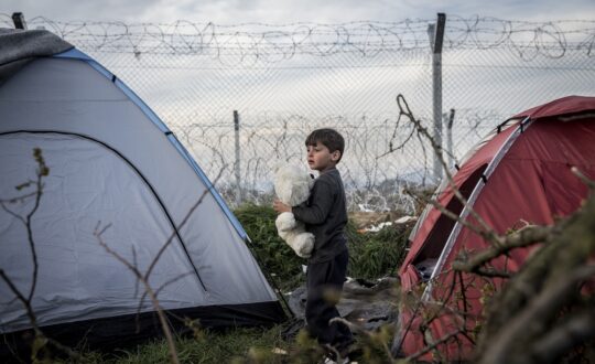 Kind zwischen Zelten am Grenzzaun zwischen Griechenland und Mazedonien (FYROM).