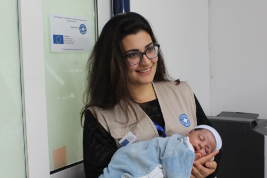 Eine Mitarbeiterin von Ärzte der Welt hält ein Neugeborenes auf dem Arm und lächelt. Ärzte der Welt leistet in Griechenland medizinische Notfallhilfe.