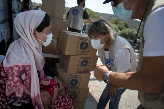 Griechenland: Eine Frau sitzt und hält ein Baby auf dem Arm. Zwei Mitarbeiter von Ärzte der Welt sind zu ihr gebeugt und reden mit der Frau. © Ärzte der Welt