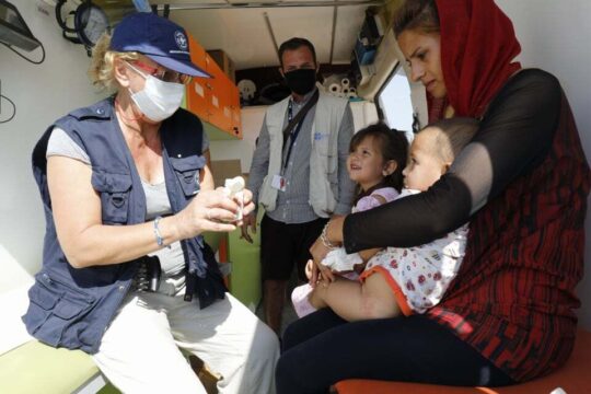 Eine Frau sitzt mit ihren zwei Kindern in einem Behandlungsbus von Ärzte der Welt in Griechenland. Vor ihnen sitzt eine Mitarbeiterin von Ärzte der Welt und versorgt die Kinder. © Yiannis Yiannakopoulos