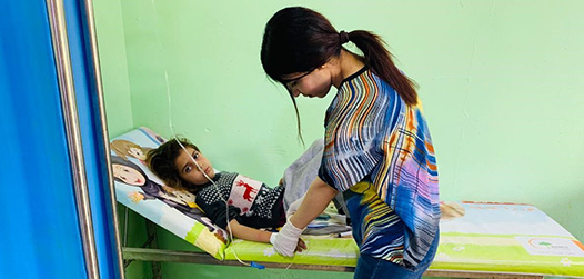 Irak: Ein kleines Mädchen liegt auf einer Untersuchungsliege und wird von einer Krankenschwester von Ärzte der Welt untersucht. © Ärzte der Welt