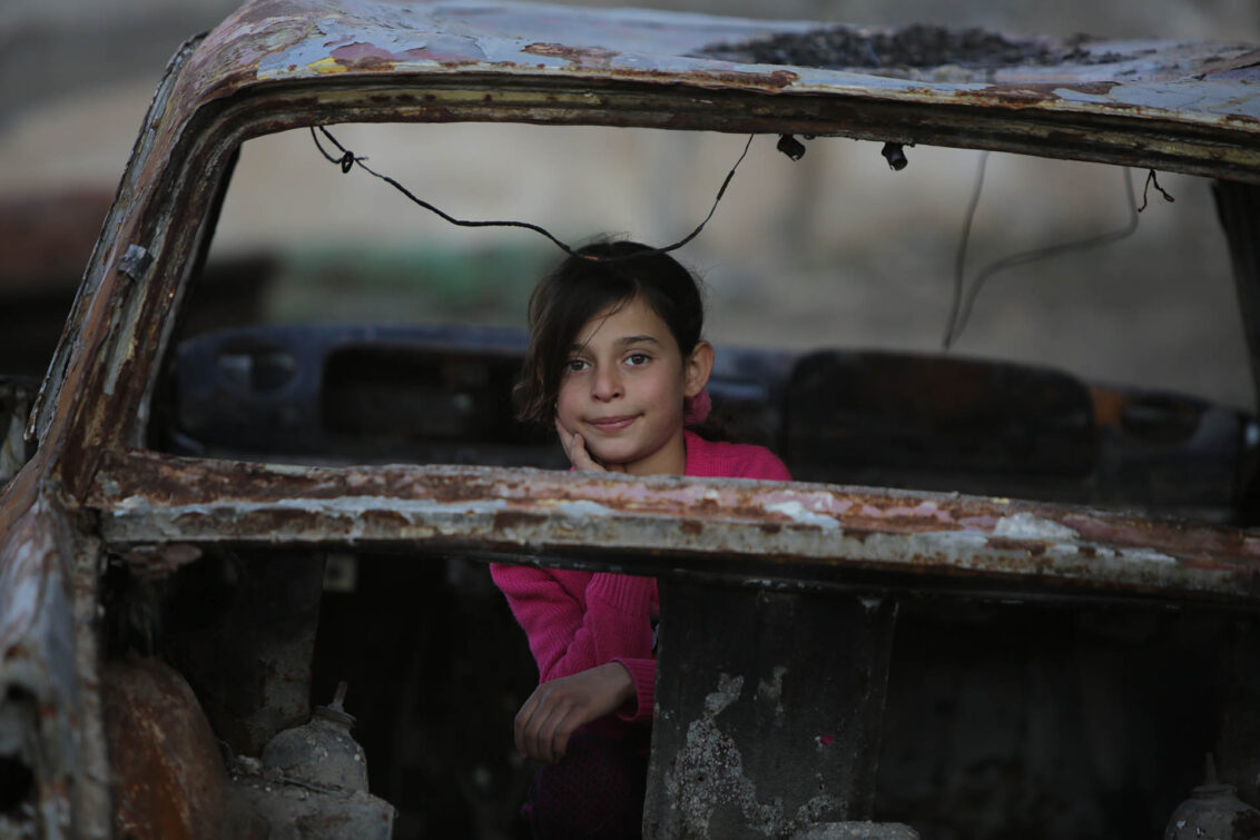 Ein junges Mädchen sitzt in den Trümmern eines zerstörten Fahrzeugs in der Region Afrin in Syrien.