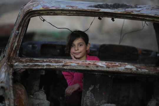 Ein junges Mädchen sitzt in den Trümmern eines zerstörten Fahrzeugs in der Region Afrin in Syrien.