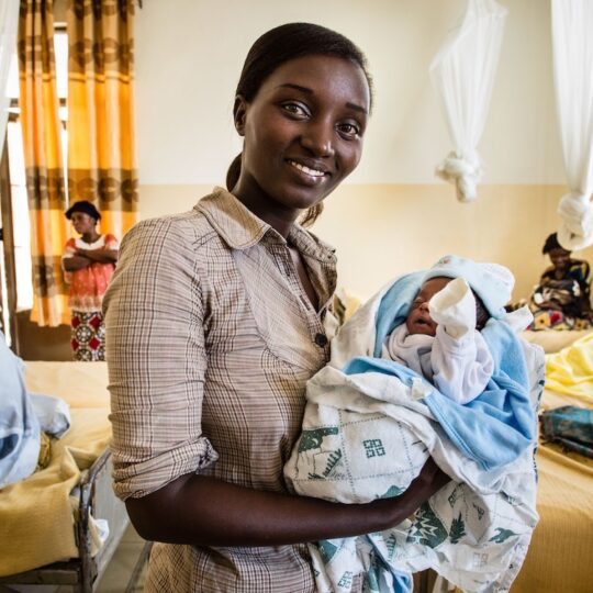 Kongo: Eine Mitarbeitern hält ein Neugeborenes und lächelt in die Kamera.