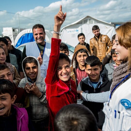 Alt-Tag: Irak: Eine Gruppe von Kindern und zwei Mitarbeiter*innen von Ärzte der Welt, lachend. © Guillaume Pinon