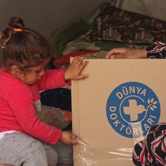 Ein kleines Mädchen aus der Türkei spielt mit einem Karton von Ärzte der Welt.
